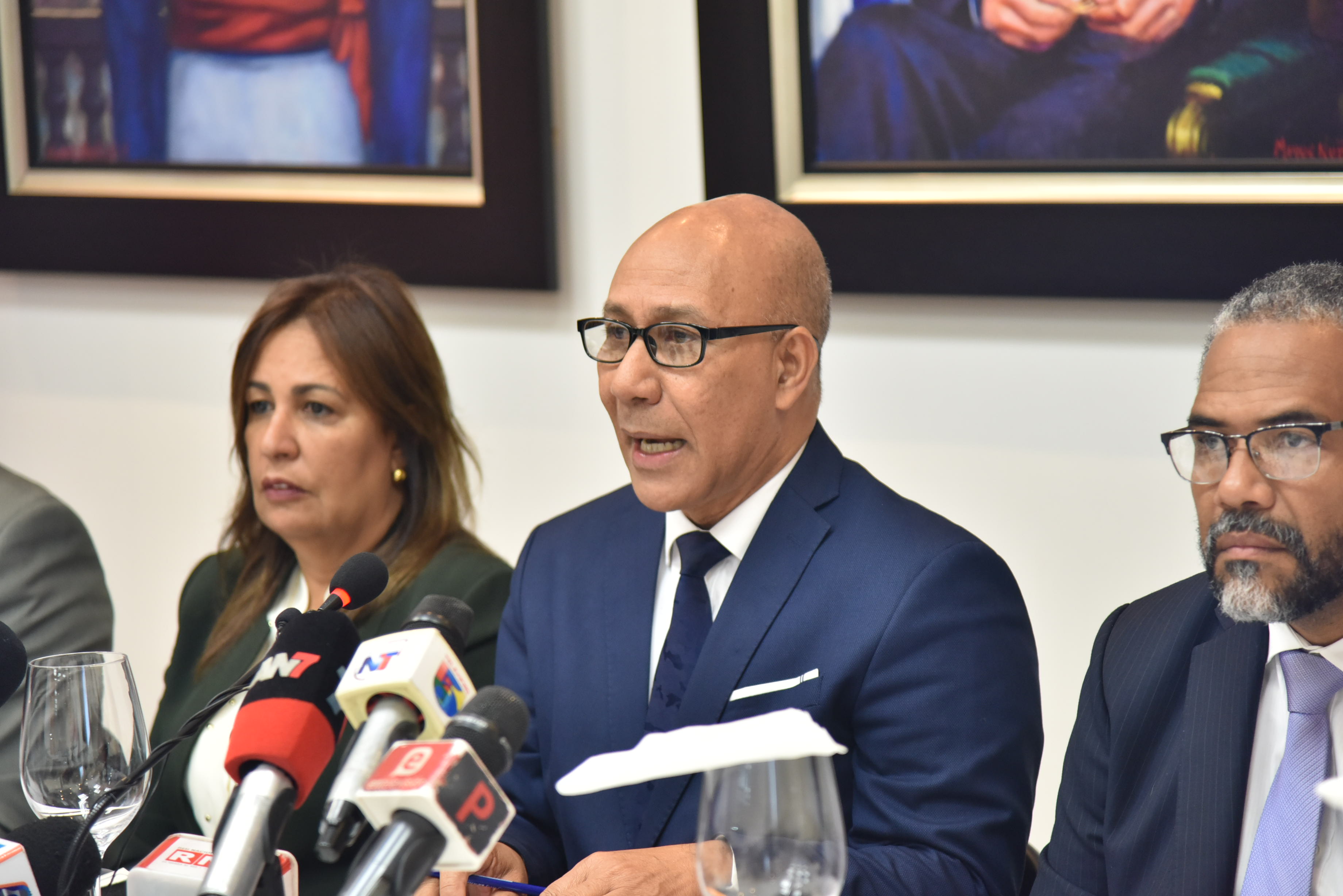  imagen Henry Santos junto a otras personalidades, sentados frente a la prensa durante rueda de prensa. 