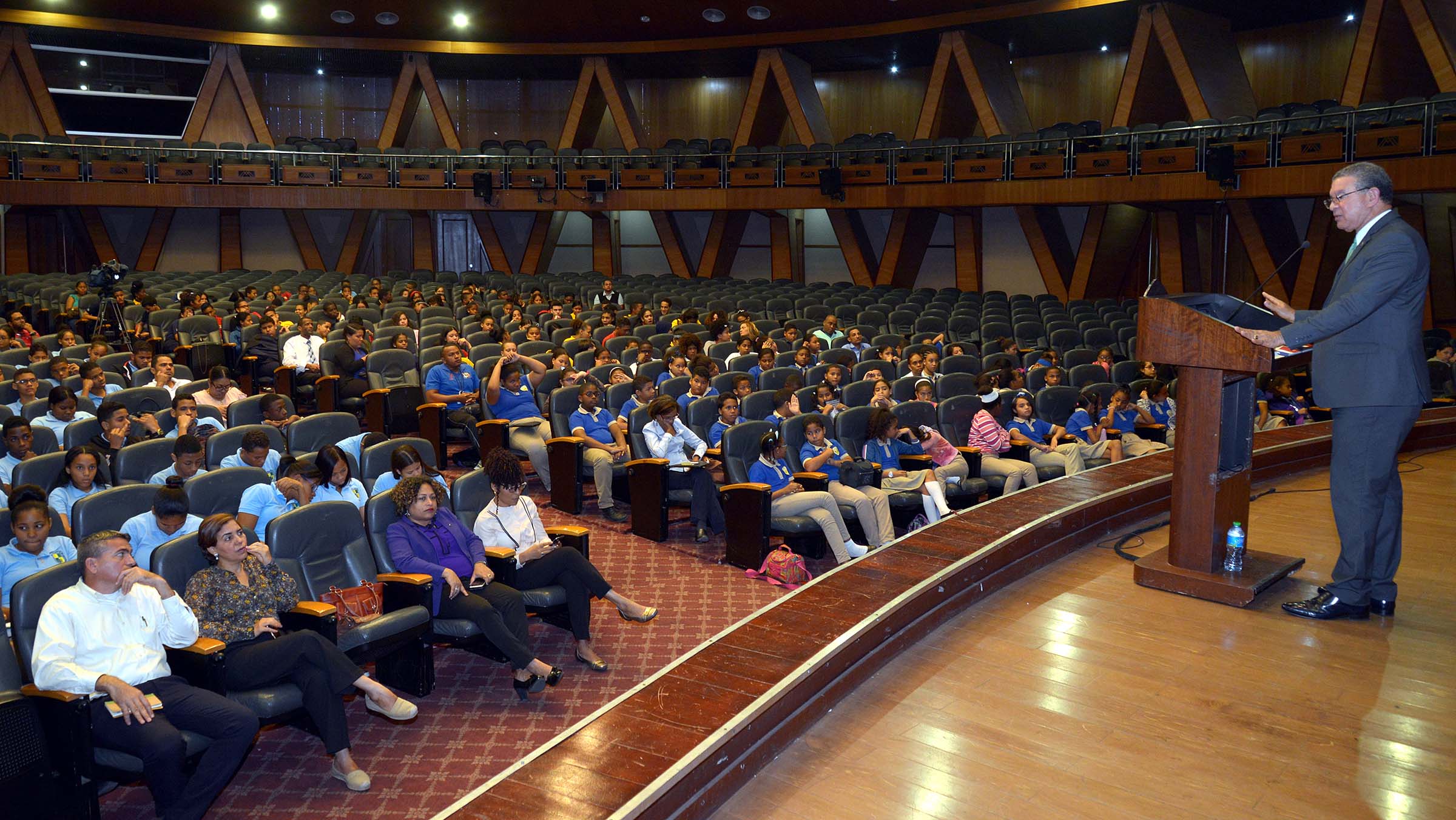  imagen Conferencista de pie en podium se dirife a estudiantes sentados 