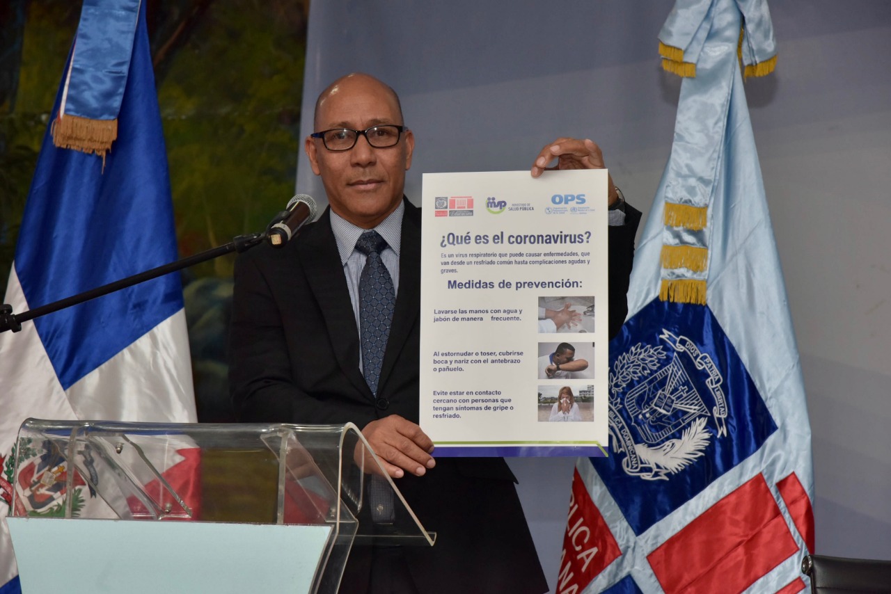  imagen Foto frontal del director de gabiete del MINERD, Henry Santos, sostiene material informativo y didactico sobre el coronavirus. 