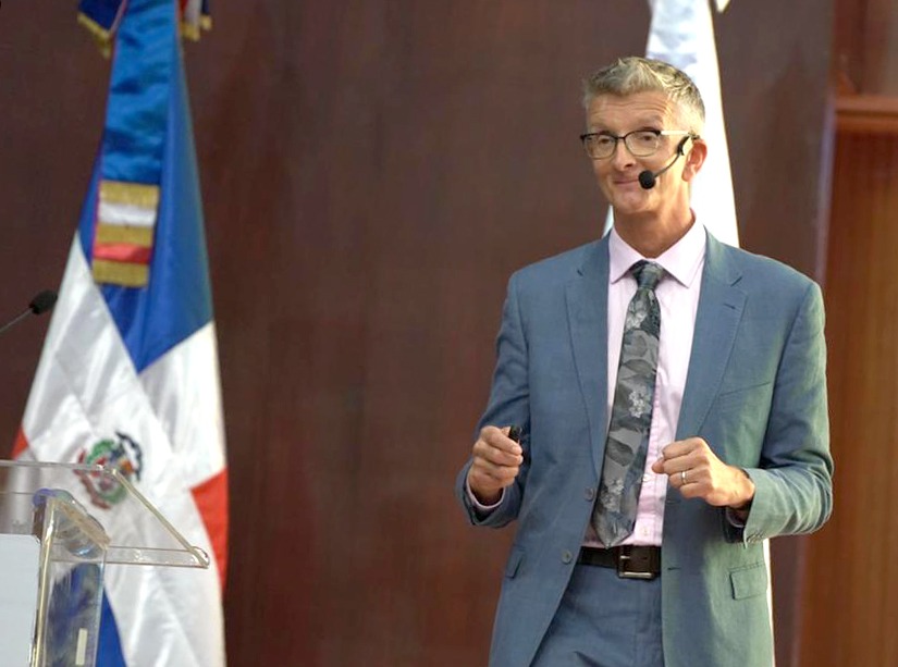  imagen Mike Major, especialista en est&aacute;ndares ling&uuml;&iacute;sticos, en el Aula Magna de la Universidad Aut&oacute;noma de Santo Domingo (UASD) de pie junto a otras autoridades educativas. 