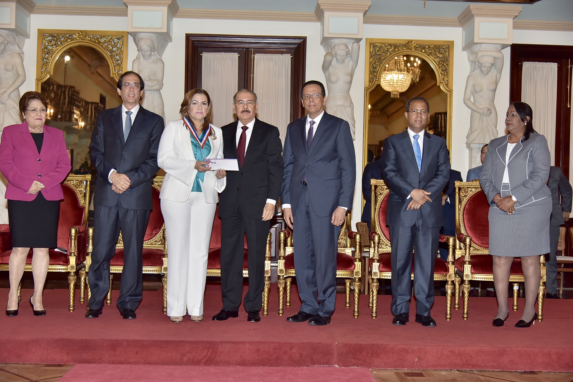  imagen De derecha a izquierda sentados, ministros Alejandrina Germ&aacute;n, Gustavo Montalvo y Presidente Danilo Medina. De pie a la derecha Ministro Antonio Pe&ntilde;a Mirabal entrega reconocimiento a&nbsp;Mar&iacute;a Marinick. 