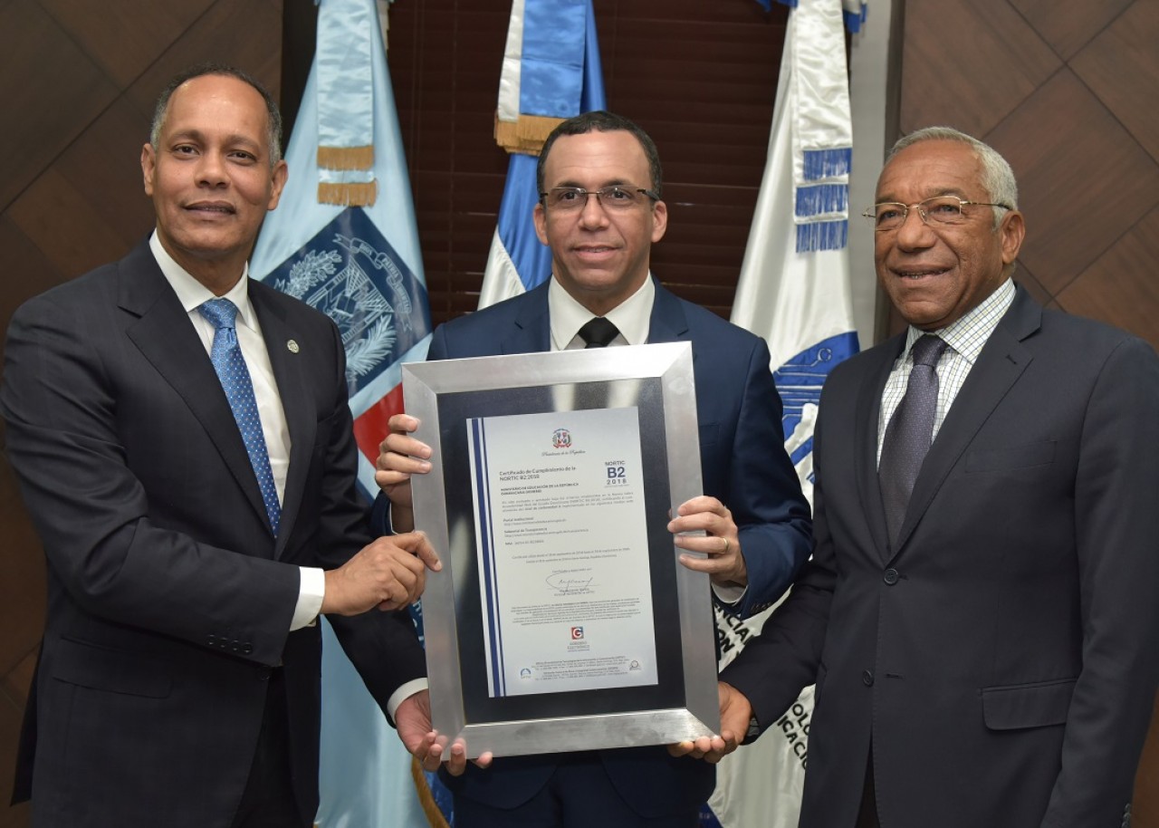  imagen Ministro Andr&eacute;s Navarro de pie sosteniendo certificaci&oacute;n Nortic B2 de manos del Director de la OPTIC, Armando Garc&iacute;a y Magino Corpor&aacute;n de CONADIS. 